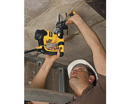 Muž vrtá do betonového stropu vrtacím kladivem.