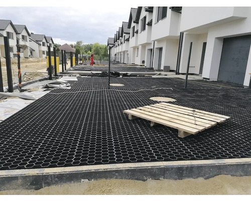 Pohled na staveniště s položenými zatravňovacími dlaždicemi před řadou domů.