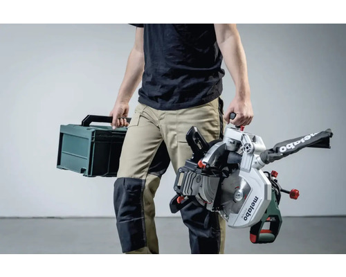 Osoba nese pokosovou pilu Metabo a kufrík s nářadím.