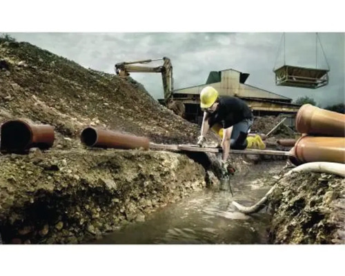 Staveniště s dělníkem, bagrem a trubkami