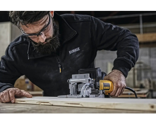 Muž používá lamelovací frézu DeWalt na dřevěné desce. Logo DeWalt.