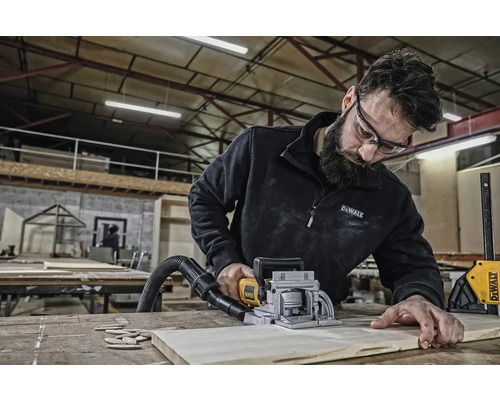 Muž používá drážkovací frézku k opracování obrobku. Nářadí a dřevo se nacházejí na pracovním stole.