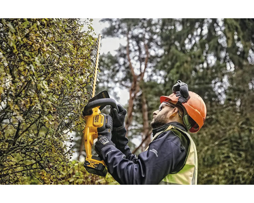 Muž stříhá živý plot pomocí akumulátorových nůžek na živý plot DeWalt
