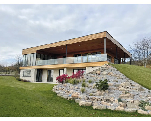Moderní dům s dřevěnou fasádou, skleněným zábradlím a kamennou zahradou ve svahu.
