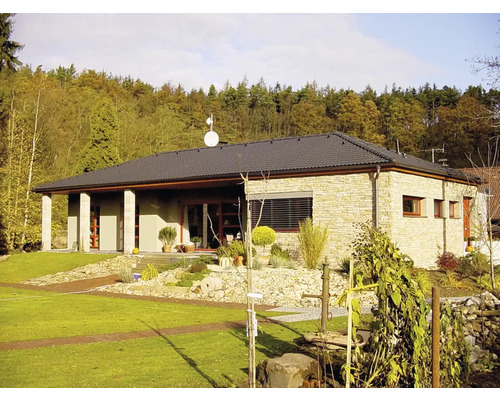 Rodinný dům s kamennou fasádou a tmavou taškovou střechou ve venkovském prostředí.