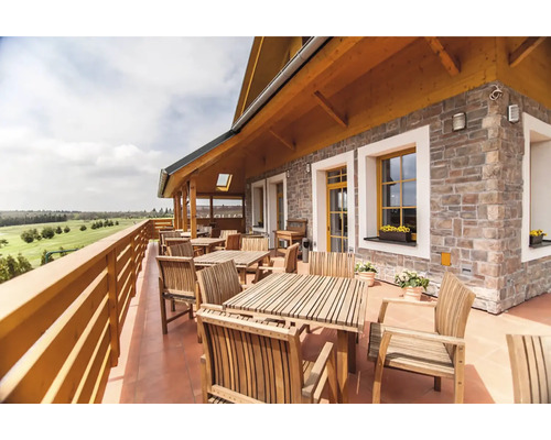 Venkovní posezení s dřevěnými stoly a židlemi na terase s výhledem do krajiny.