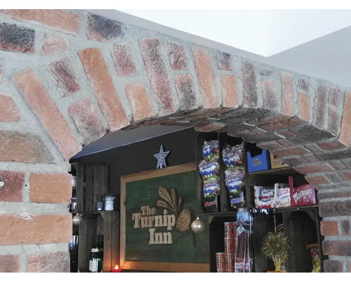 Zděný oblouk nad barem s nápisem The Turnip Inn a policemi s občerstvením.