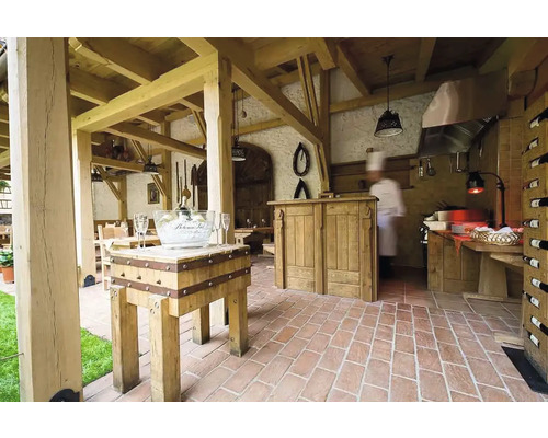 Scéna restaurace s dřevěnou konstrukcí, stoly, židlemi, cihlovou podlahou a barem.