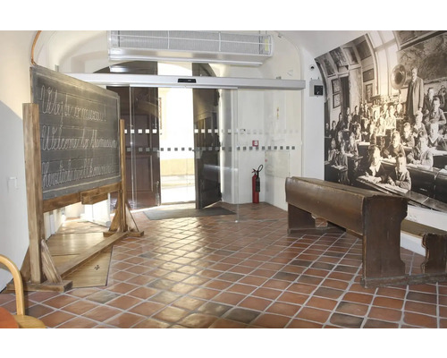 Vstupní prostor s břidlicovou tabulí, školní lavicí a historickou fotografií školní třídy