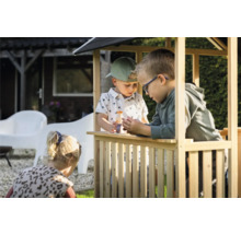 Tři děti si hrají v dřevěném hracím domku na zahradě.