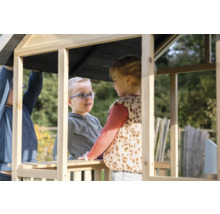 Dvě děti si hrají v neošetřeném dřevěném hracím domku na zahradě.