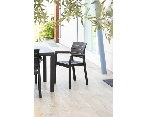 Plastová zahradní židle s područkami vedle zahradního stolu