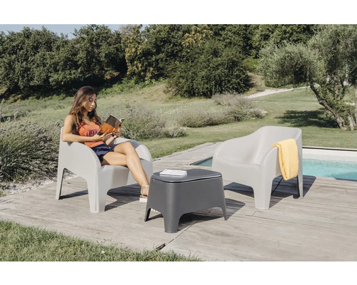 Zahradní scéna se dvěma křesly, odkládacím stolkem a ženou čtoucí knihu