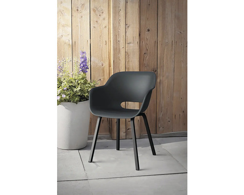 Plastová zahradní židle s područkami před dřevěnou stěnou