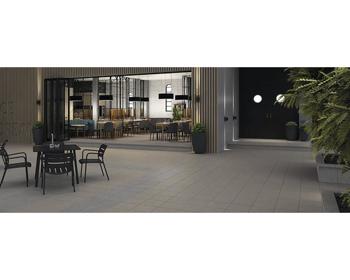 Venkovní posezení restaurace s dlážděnou podlahou, stoly a židlemi.