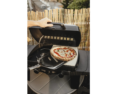Příprava pizzy na plynovém grilu s pizza kamenem a lopatkou na pizzu.