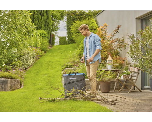 Muž stříhá zahradní odpad zahradními nůžkami a zahradním pytlem na zahradě.