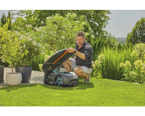 Muž otevírá víko robotické sekačky na trávníku