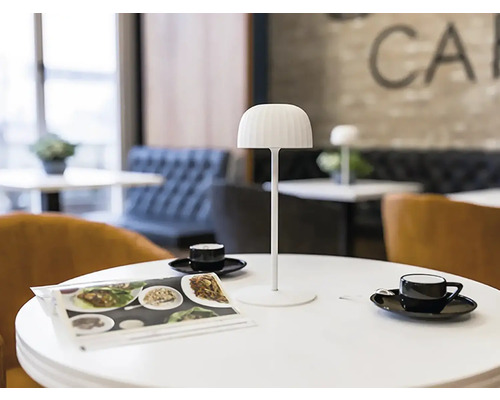 Scéna s bílou stolní lampou, časopisy a šálky na stole v kavárně.