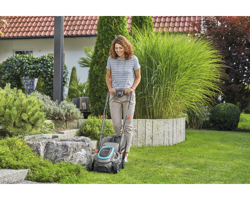 Žena používá sekačku na trávu na zahradě.