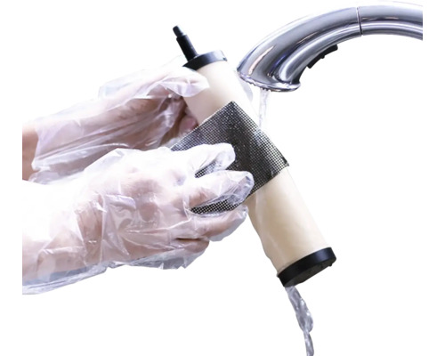 Osoba čistí vodní filtr pod vodovodním kohoutkem smirkovým papírem