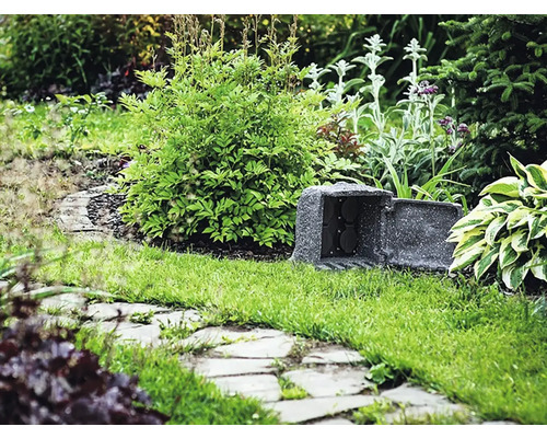 Zásuvkový sloup v zahradě mezi rostlinami a trávou