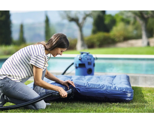 Žena nafukuje matraci elektrickou pumpou na zahradě.