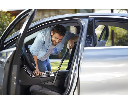 Muž čistí interiér auta vysavačem.