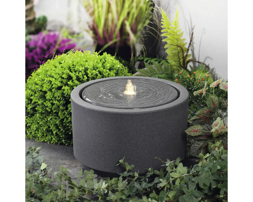 Kulatá pokojová fontána z kameniny s vodní hrou na zahradě.