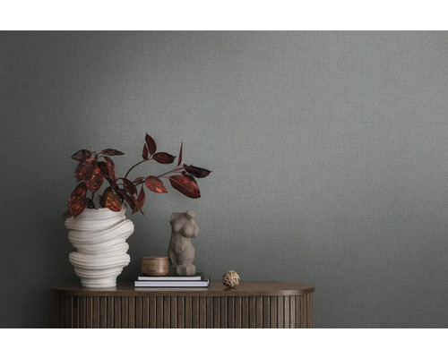 Detailní záběr šedé vliesové tapety se strukturou v pozadí místnosti s komodou a dekorací