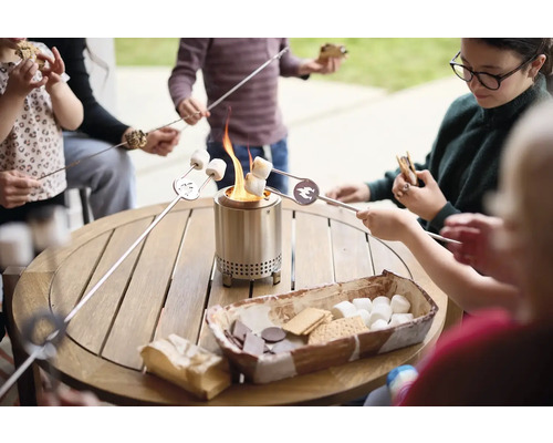 Rodina opéká marshmallows na stolním grilu, na stole jsou přísady na s''mores.