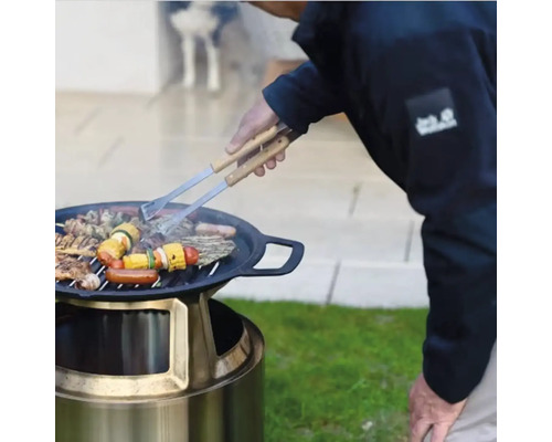 Venkovní gril s grilovanými potravinami a grilovacími kleštěmi na zahradě