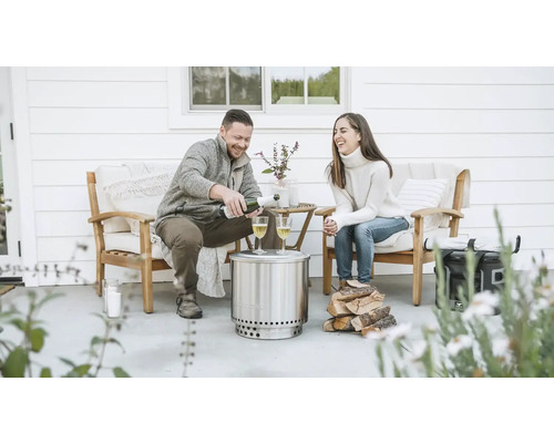 Scéna s párem na terase s ohništěm Solo Stove, dřevem a nápoji.