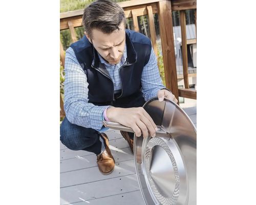 Osoba montuje kulatý ohniště stříbrné barvy venku.