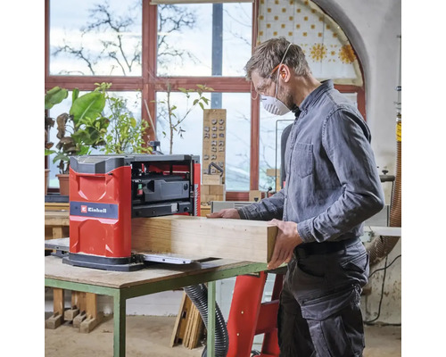 Muž pracuje s hoblovkou Einhell na kusu dřeva v dílně.