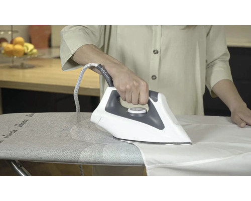 Osoba žehlí bílou košili žehličkou na žehlicím prkně.