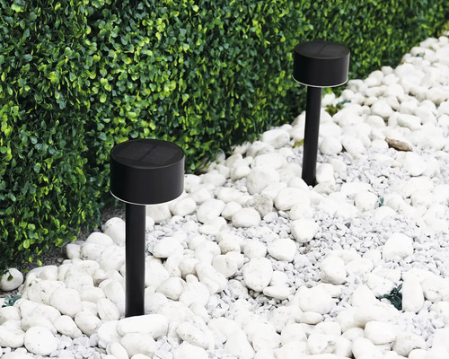 Dvě černá solární světla v zahradě mezi bílými kameny a zeleným živým plotem