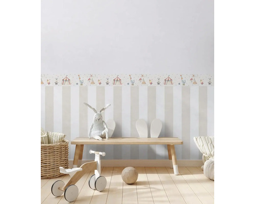 Dětský pokoj s pruhovanou tapetou a bordurou s motivem cirkusu, s dřevěnou lavicí, hračkami a dekorací