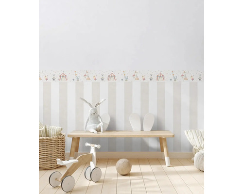 Dětský pokoj s pruhovanou tapetou, cirkusovou bordurou, hračkami a dřevěnou lavicí.