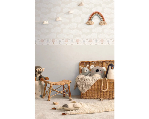 Zdobený dětský pokoj s tapetou s oblaky, nástěnnou dekorací s duhou, ratanovou stoličkou a hračkami v košíku.