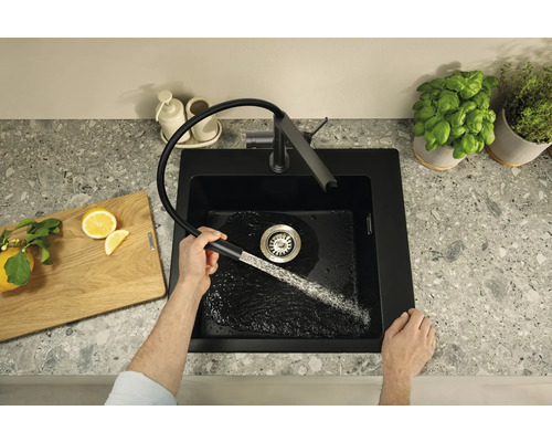 Černý kuchyňský dřez s vodovodní baterií a mužem, který ovládá kohoutek
