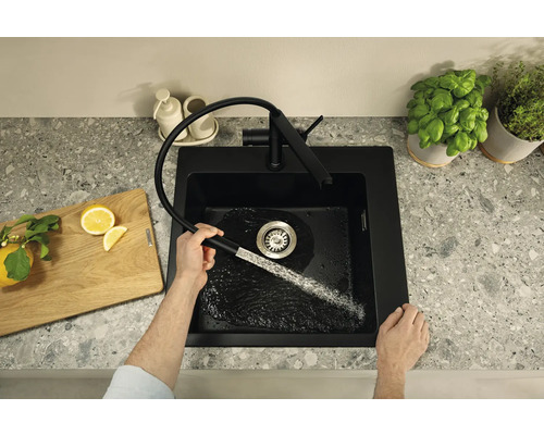 Černý kuchyňský dřez s výsuvnou baterií v moderním designu na pracovní desce, zatímco do dřezu teče voda.