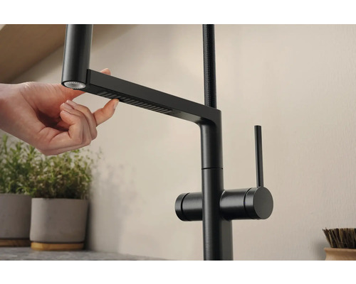 Detailní záběr na černou kuchyňskou baterii s výsuvnou sprchou ovládanou rukou.