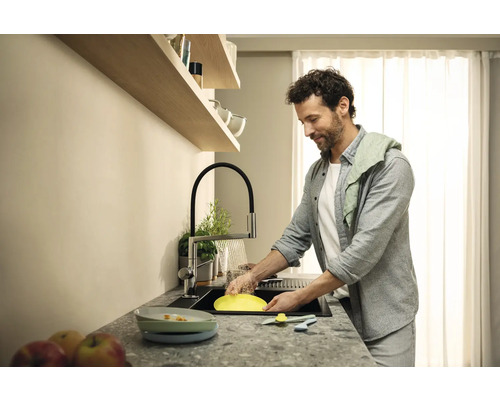 Muž myje nádobí v moderní kuchyni s dřezem, kuchyňskou baterií a odkapávačem