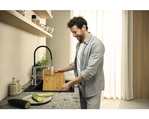 Muž myje dřevěné prkénko v moderní kuchyni s dřezovou baterií