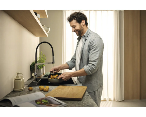 Muž myje brambory v umyvadle s kuchyňskou baterií v moderní kuchyni.