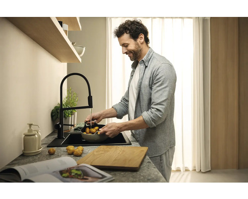 Muž myje brambory v moderní kuchyni s černým dřezem a baterií.