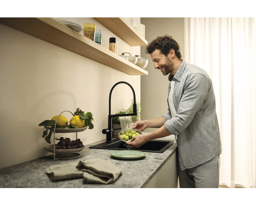 Muž myje ovoce v kuchyňském dřezu s černým kohoutkem