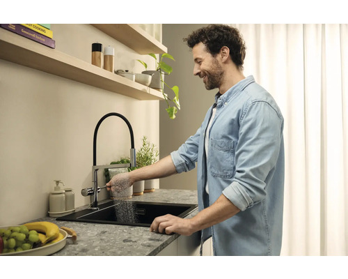 Muž používá kuchyňskou baterii se sprchou u moderního dřezu