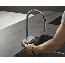 Osoba ovládá chromovanou kuchyňskou baterii u dřezu